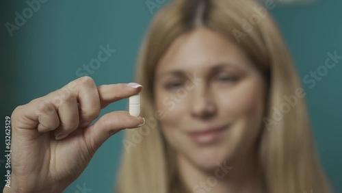 Close up portrait of a blonde woman holding a pill in her hand, smiling and nodding. Slow motion HDR BT2020 HLG Material. photo