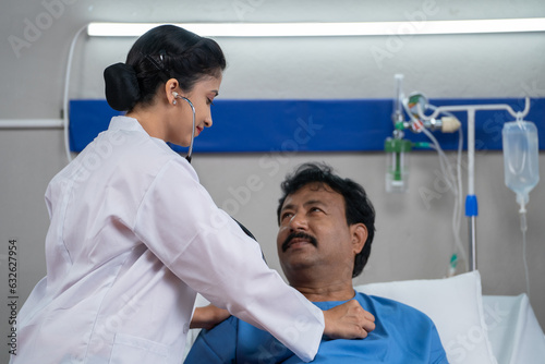 Indian doctor examining or checking admitted sick patient by using stethoscope at hospital ward - concept of Healthcare Professional  medical assessment and treatment.