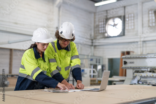 Man and woman engineer with laptop discussing drawing design new product wooden furniture in factory.