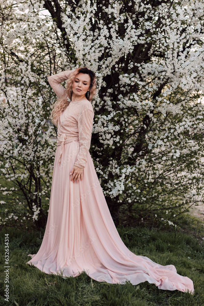 A girl stands near a flowering tree in spring. Cherry blossoms