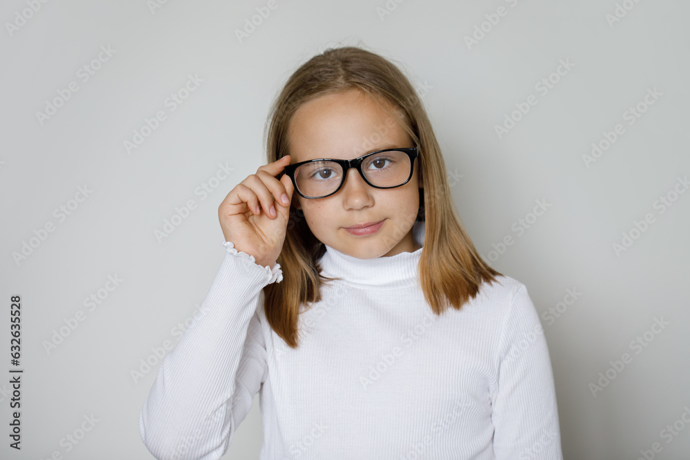 Pretty smart young brunette girl in glasses looking at camera on white wall background, studio portrait