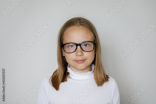 Clever child girl in glasses looking at camera on white background, studio portrait