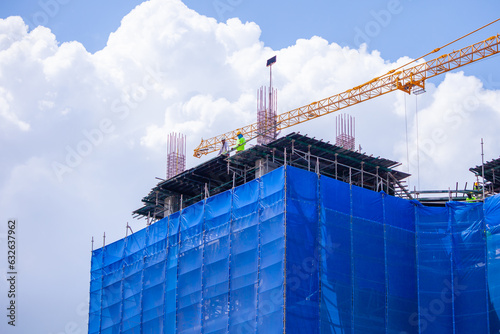 A blue slan surrounds the building under construction. Crane. Crane for lifting things in construction against sunset sky atmosphere. communities and large industrial construction zones.	 photo