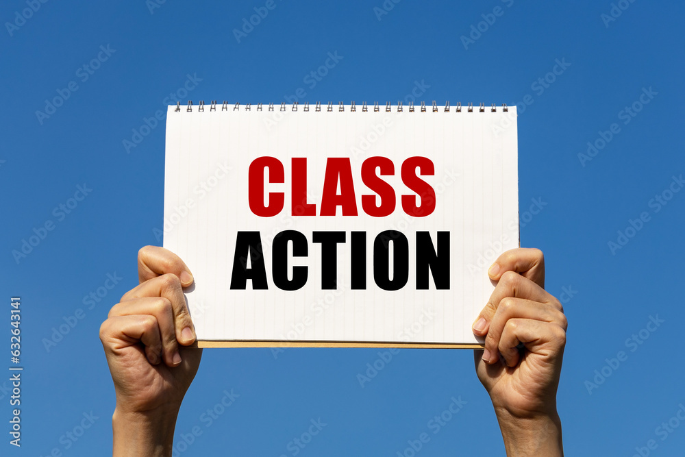 Class action text on notebook paper held by 2 hands with isolated blue sky background. This message can be used as business concept about class action. Class action text on notebook paper held by 2 hands with isolated blue sky background. This message can be used as business concept about class action.