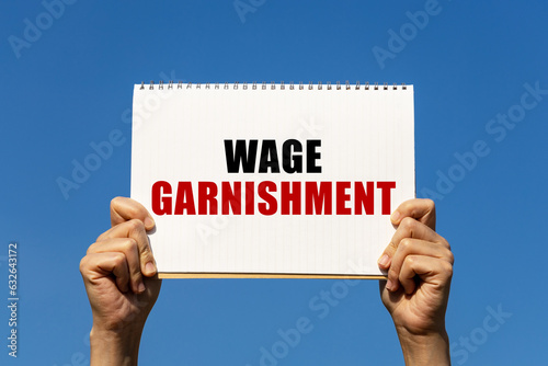Tableau sur toile Wage garnishment text on notebook paper held by 2 hands with isolated blue sky background