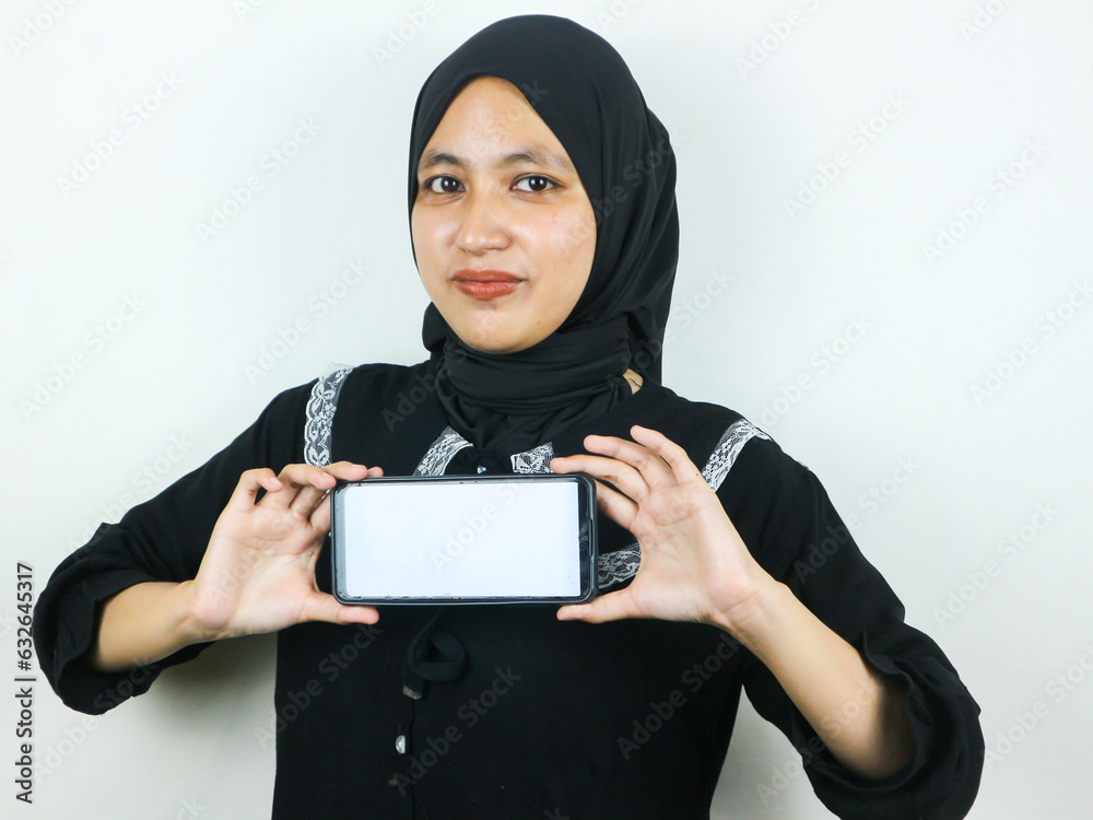 Young Muslim woman in hijab smiling showing mobile phone blank screen recommending App Young Muslim woman in hijab smiling showing mobile phone blank screen recommending App