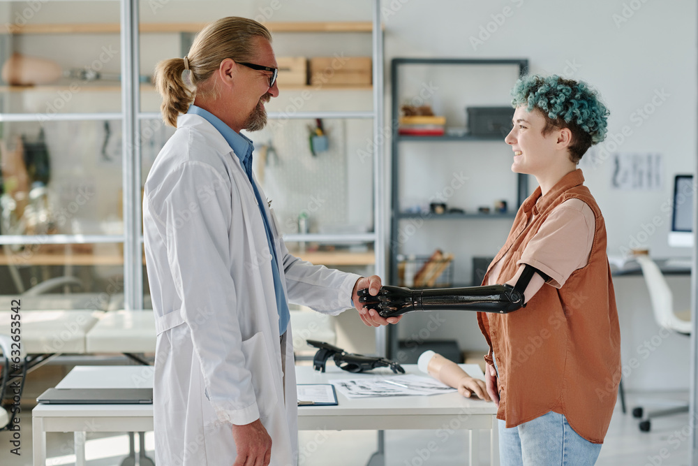 Side view portrait of young woman with bionic prosthetic arm shaking hands with doctor in clinic Side view portrait of young woman with bionic prosthetic arm shaking hands with doctor in clinic