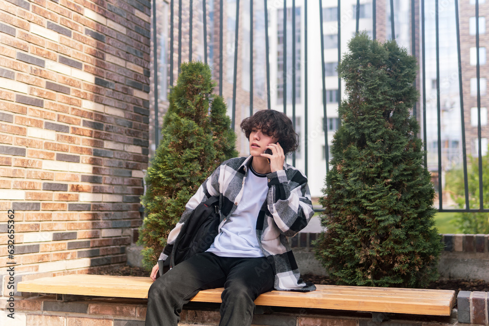 young man talking on the phone while sitting on a bench in the city young man talking on the phone while sitting on a bench in the city