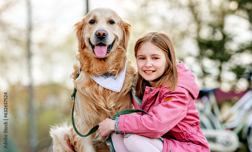 Girl with golden retriever dog outdoors in sunny day portrait. Female child kid hugging pet doggy labrador at street