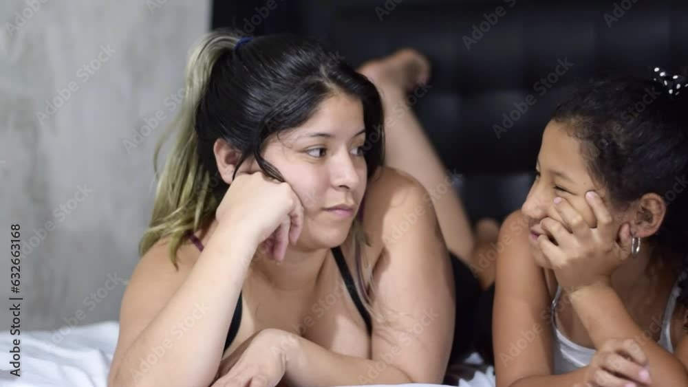young latina mother lying on bed talking to her young daughter, giving her life advice. concept of motherhood young latina mother lying on bed talking to her young daughter, giving her life advice. concept of motherhood