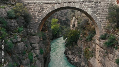 Low flight above water flowing in wild creek between rough rocky banks. Fly under stone road bridge. Turkey. 