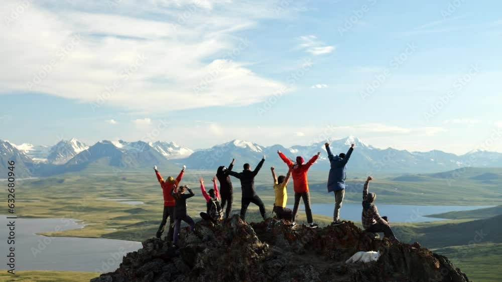 Traveling group together raise arms and joy achievement on mountain top. Happy hikers celebrate high win, success on cliff peak at scenic landscape view