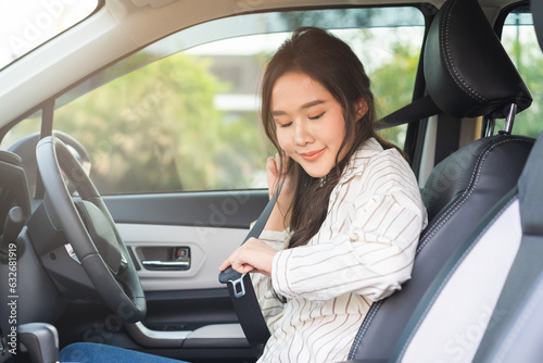 Happy smile brunette asian young woman hand fastens a seat belt sitting in front of car before driving, vehicle for travel, trip take a safe journey, attractive driver with safety belt, transportation