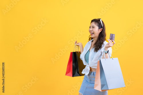 Portrait of young Asian attractive women holding credit cards and shopping bags enjoy purchasing gifts in department store isolated yellow studio background, happy smile shopper summer lifestyle