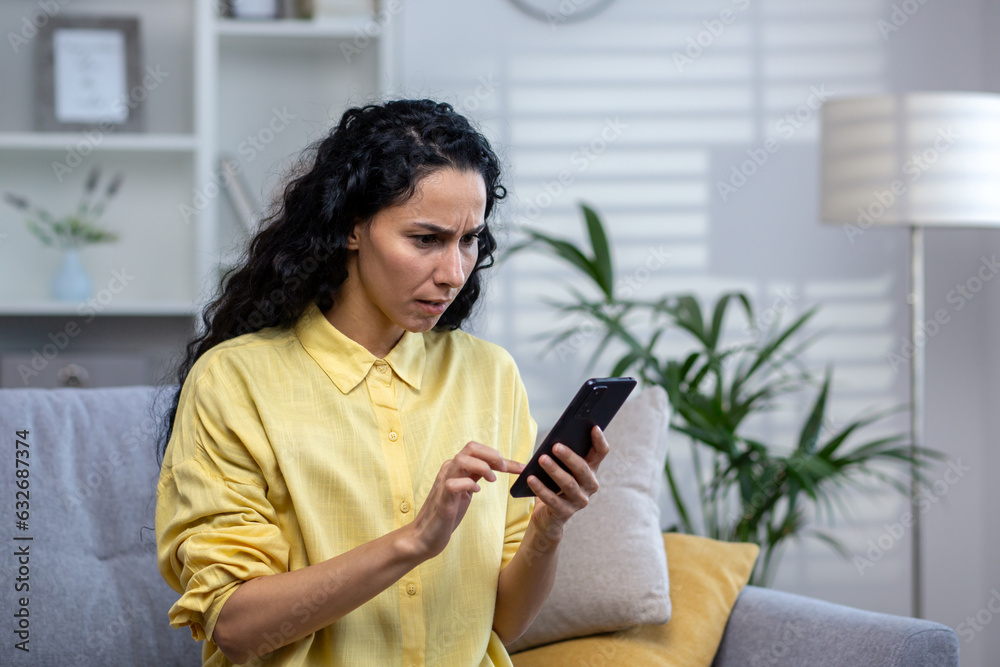 Upset and disappointed serious thinking woman alone at home using app on phone close up, hispanic sitting on sofa in living room at home. Upset and disappointed serious thinking woman alone at home using app on phone close up, hispanic sitting on sofa in living room at home.