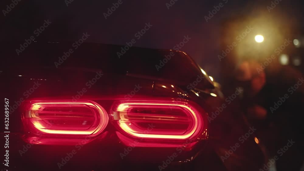 Black sports car tail light glowing in the dark of a night city
