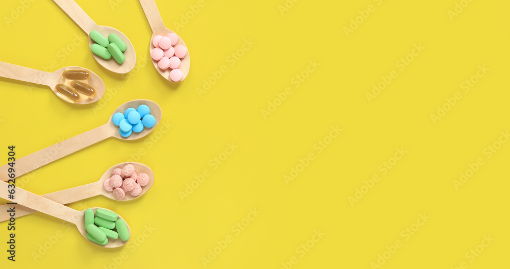 Vitamins on a yellow background, top view. Pills of different colors in wooden spoons, flat lay. Medicines, vitamins and dietary supplements. Banner with place for text