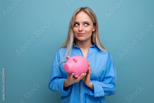 pensive blond girl with an idea holding a piggy bank on a blue isolated background