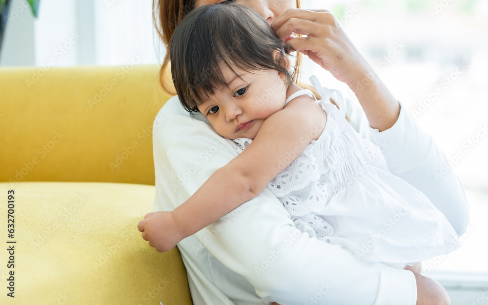 Mother holding and hugging adorable caucasian little baby daughter girl, playing together, smiling with love, happiness and warmth, staying in comfortable living room at home. Family and Kid Concept.