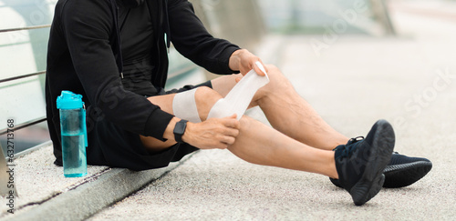 Sportsman suffering with knee pain during workout  putting bandage