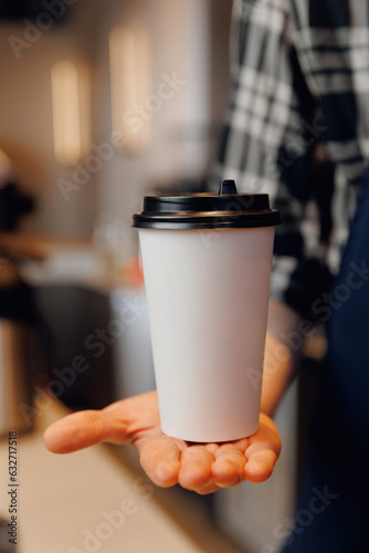 Barista holding white cardboard paper cup with fresh coffee to go