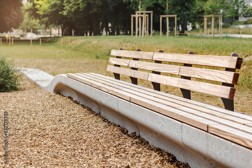 Bench in Green Park with Wood Chips Covering Ground at Children Playground. Modern Wooden Bench in Relax Zone Area on Nature Background. photo