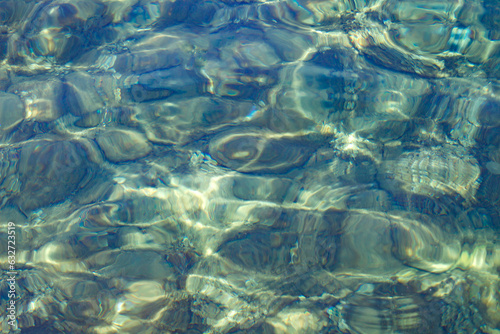 Bottom of stones in sea through clear water with waves