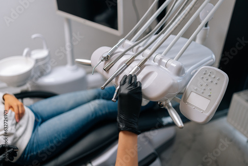 Close-up side view of unrecognizable female stomatologist in rubber gloves taking electrical dental drill from set of dental tools to treat patient with toothache, in modern dentistry clinic.