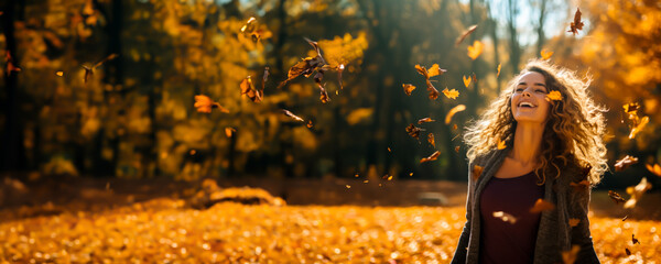 Joyful smiling Woman throwing leaves into the air in a park in the autumn. Colors are warm orange and yellow. Concept of fall colors, fashion and happiness. Shallow field of view.