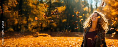 Joyful smiling Woman throwing leaves into the air in a park in the autumn. Colors are warm orange and yellow. Concept of fall colors, fashion and happiness. Shallow field of view.
