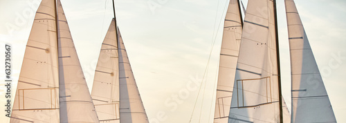 the tops of several sails are illuminated by the sun at sunset, clear sky, masts