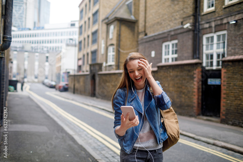 Young woman using a smart phone while walking down a sidewalk in London