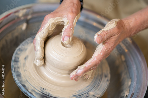 Woman working on potter's wheel in a pottery workshop, creating clay pot.