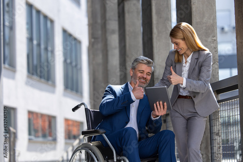 Woman and man in wheelchair working together, joint architecture project, using laptop and tablet.