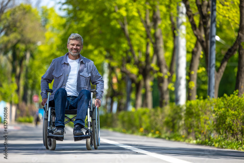Handicapped man in wheelchair riding on street road, outdoor leisure for disable guy. © zinkevych