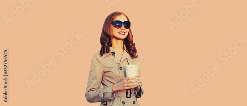 Portrait of beautiful woman with coffee cup wearing coat, sunglasses on brown background © rohappy
