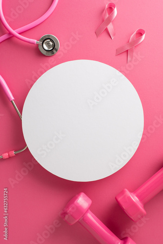 Proactive breast cancer awareness theme. Top view vertical shot of pink ribbon emblems, stethoscope, dumbbells on pink backdrop. Circular space for text or promotion