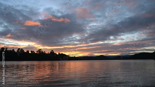 Vibrant Sunset Cloudscape  on reflecting tree lined lake 
