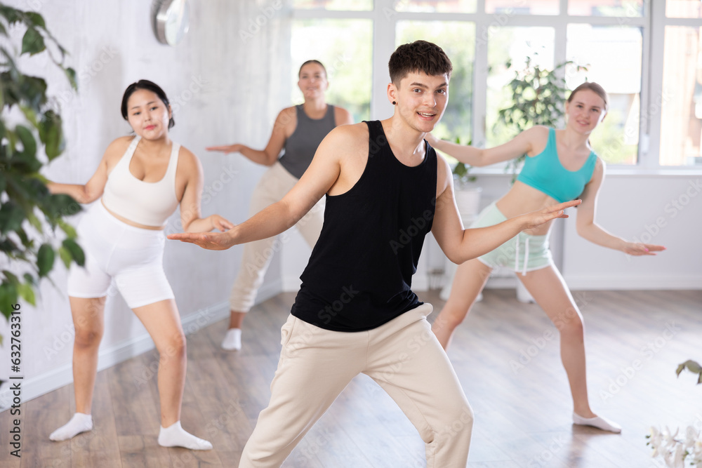 Cheerful sporty girl and guy practicing energetic dance moves with group in choreography class