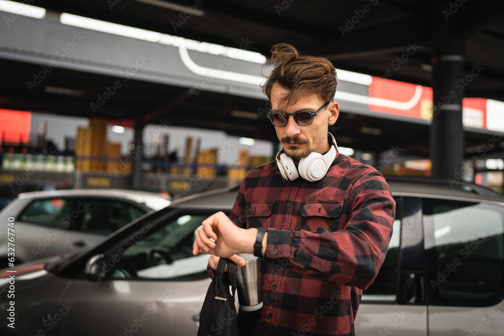 One young adult man stand at parking lot checking time on wristwatch