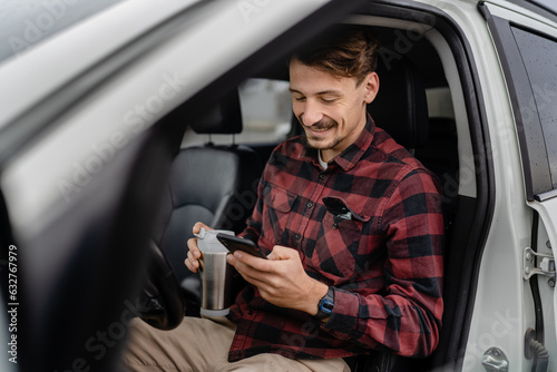 man hold cup with coffee use mobile phone sit in the car take a brake