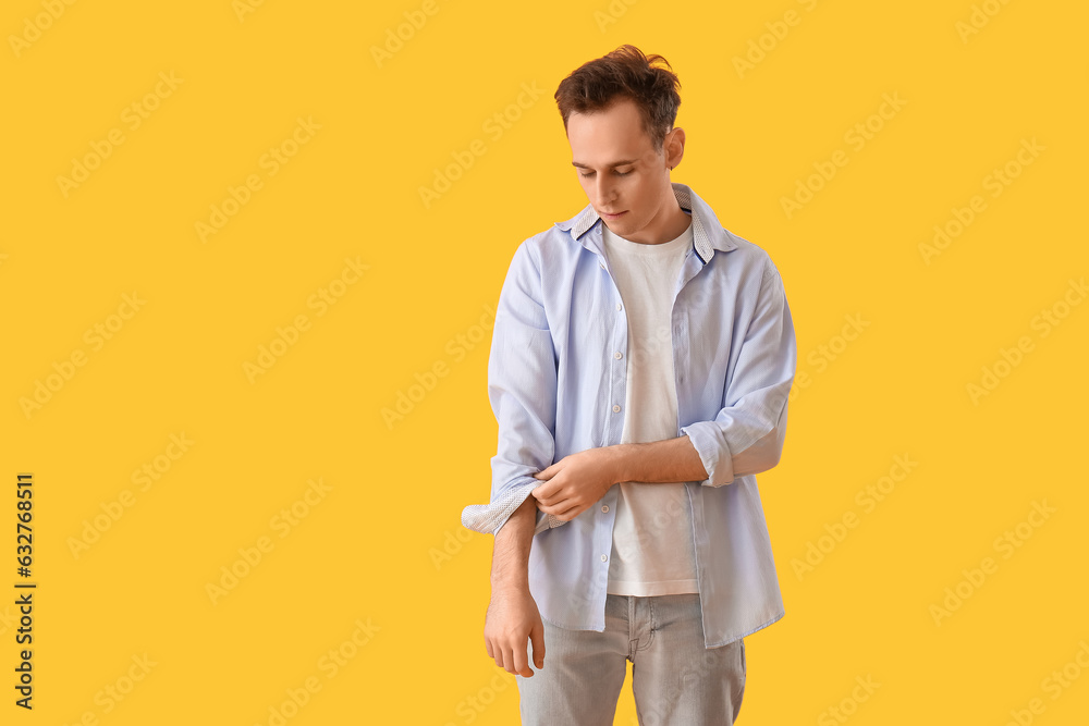 Young man rolling up his sleeve on yellow background Young man rolling up his sleeve on yellow background