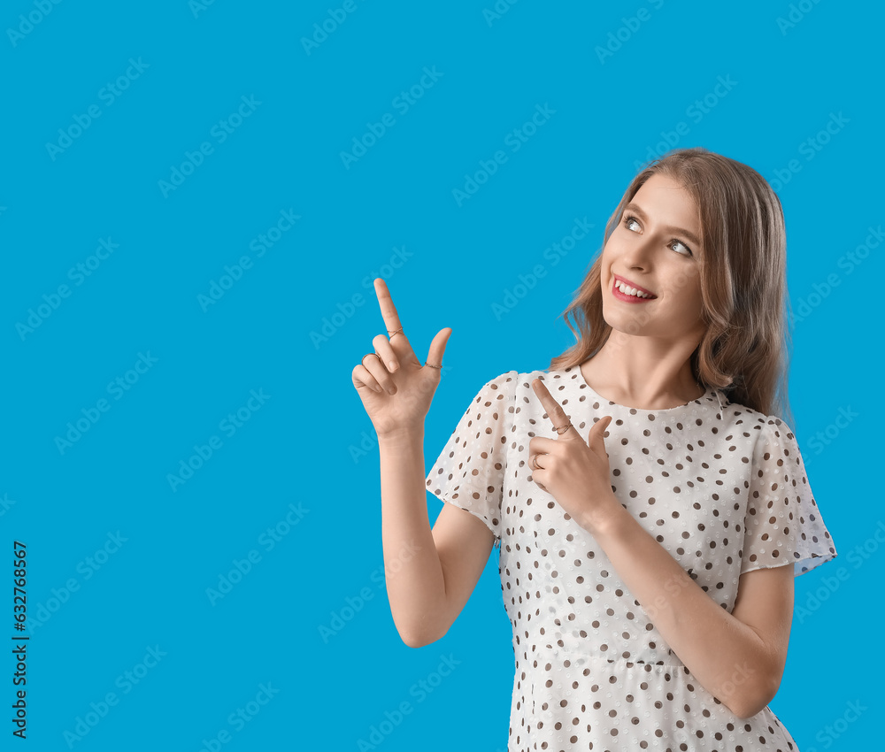 Young woman pointing at something on blue background Young woman pointing at something on blue background