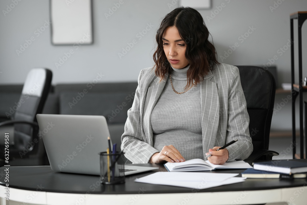 Young pregnant woman working at table in office Young pregnant woman working at table in office