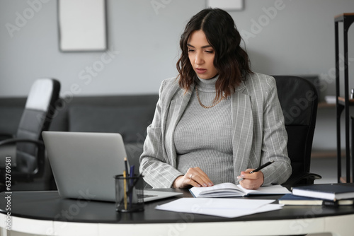 Young pregnant woman working at table in office
