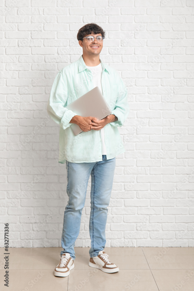 Male programmer with laptop near white brick wall Male programmer with laptop near white brick wall
