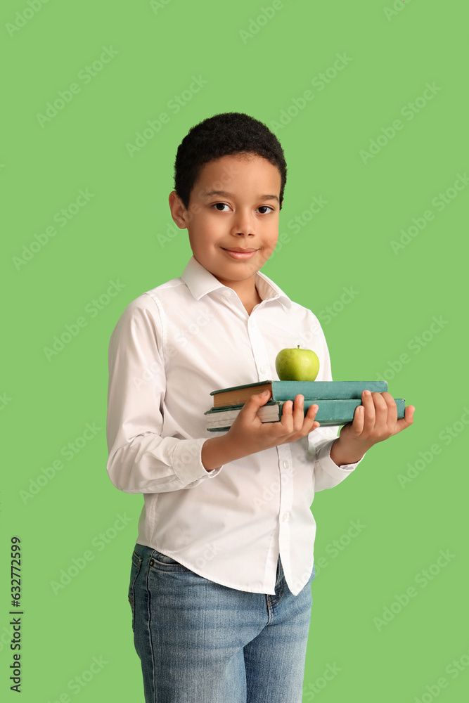 Little African-American schoolboy with books and apple on green background Little African-American schoolboy with books and apple on green background