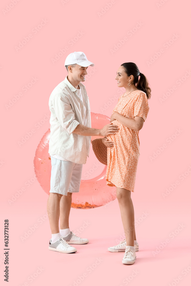 Young pregnant couple with inflatable ring on pink background Young pregnant couple with inflatable ring on pink background