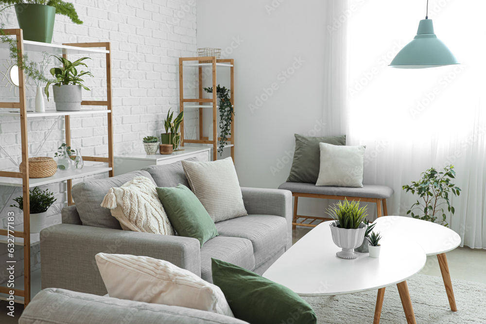 Fototapeta premium Interior of light living room with grey sofa, coffee table and houseplants