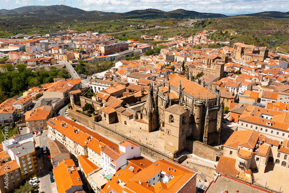 Drone view of picturesque cityscape of historical part of Placencia surrounded by ancient fortress wall overlooking tiled roofs of houses and medieval gothic cathedral on sunny spring day, Spain